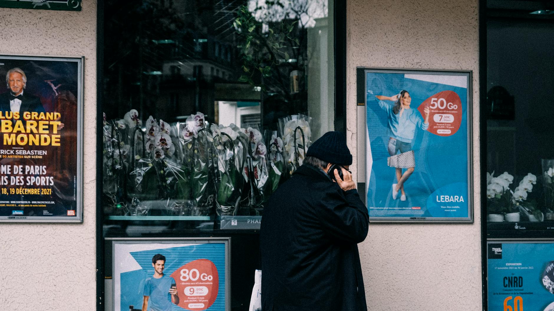 A person holding up their phone to photograph a colorful event poster on a city street in daylight