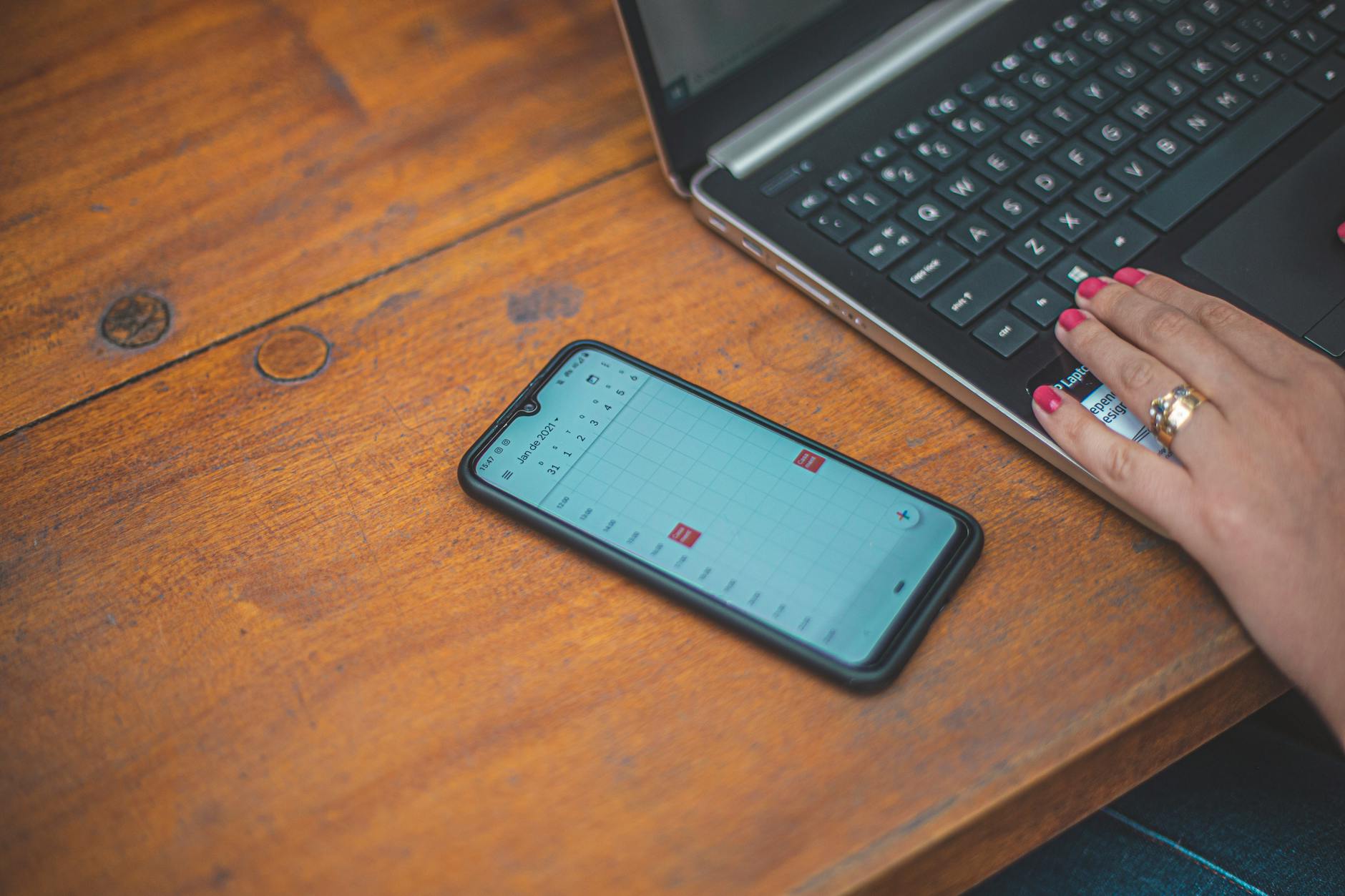 A phone resting on a wooden table showing a clean calendar view with an upcoming event, natural light