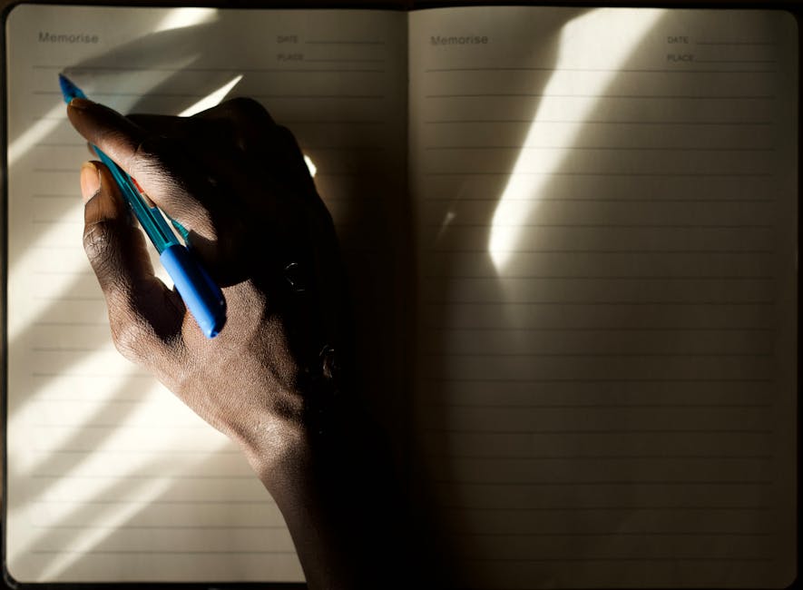 A person writing in a journal by a bright window with a cup of tea on the desk