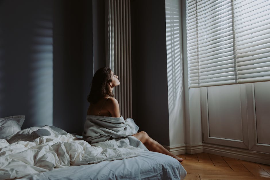 A sunlit bedroom with white bedding and a glass of water on a minimal nightstand in early morning light
