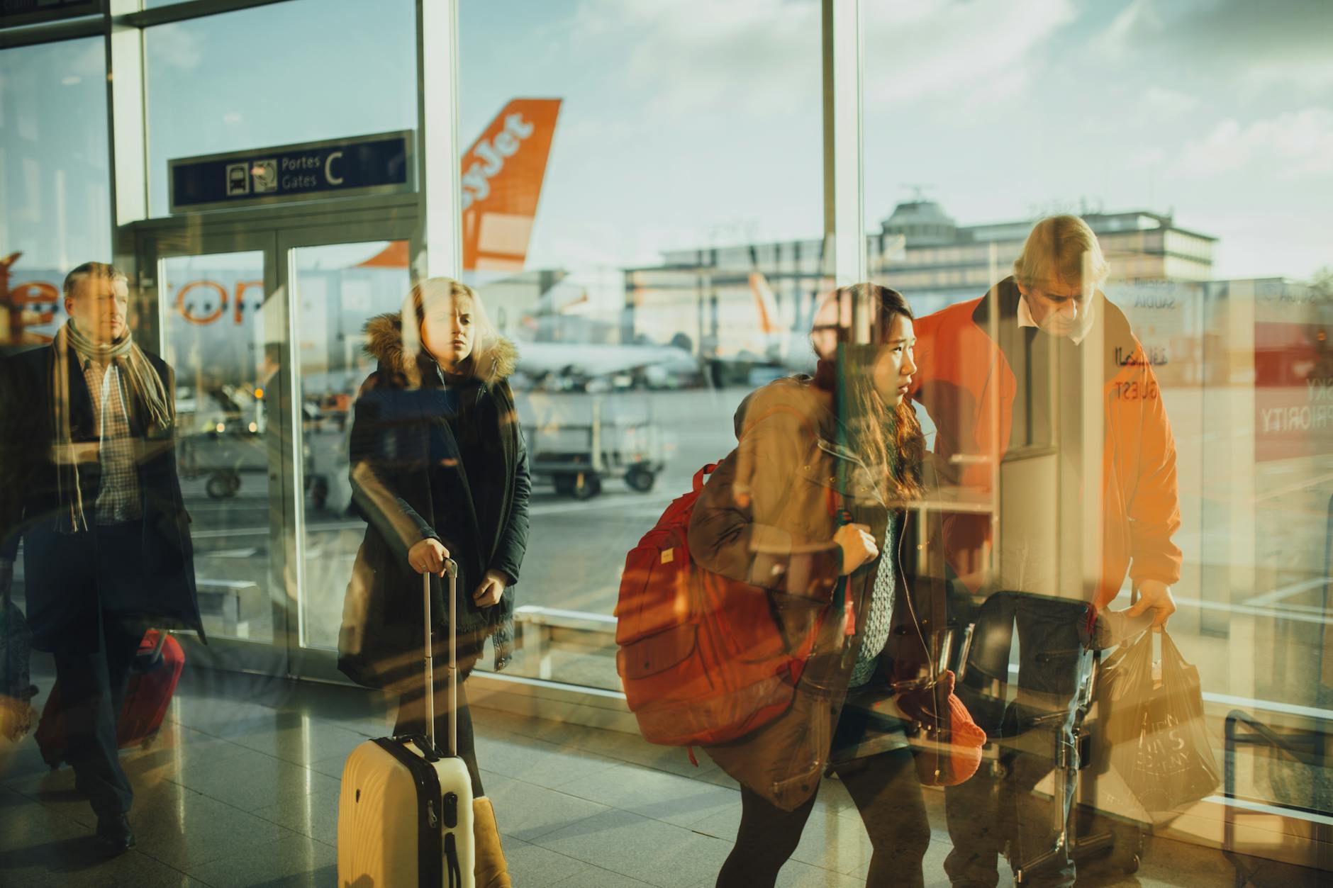 A traveler sitting at an airport gate checking their phone, large windows showing an airplane in the background