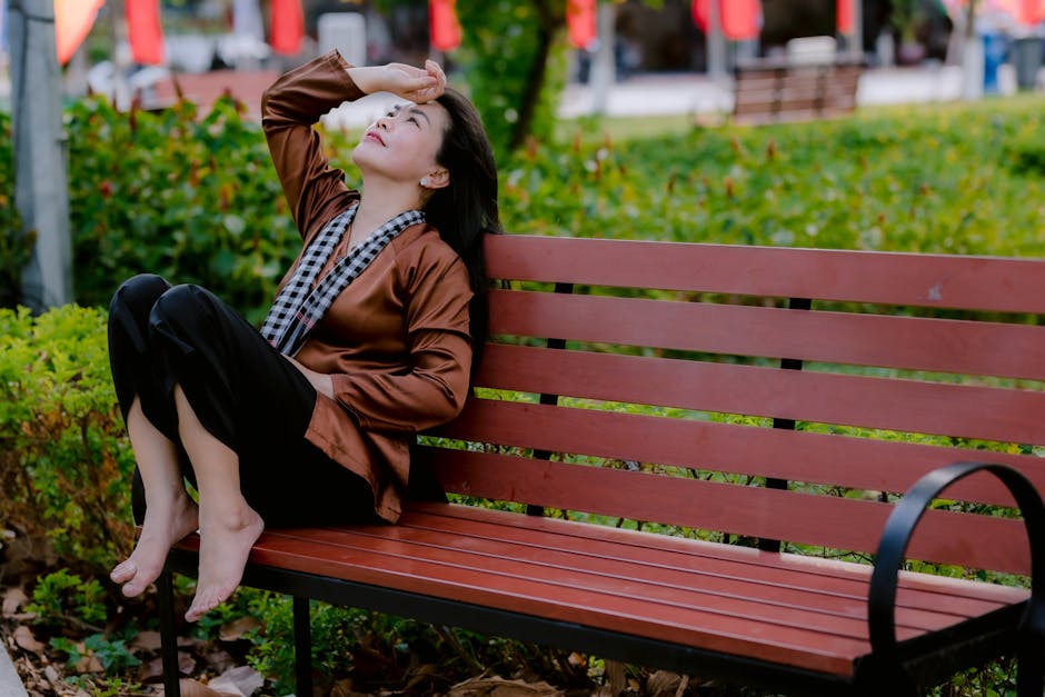 A person relaxing on a park bench during a break, phone in pocket, watching trees sway