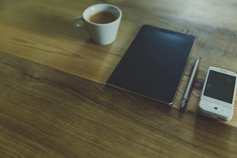 A smartphone resting on a warm wooden table next to an open notebook in soft morning light